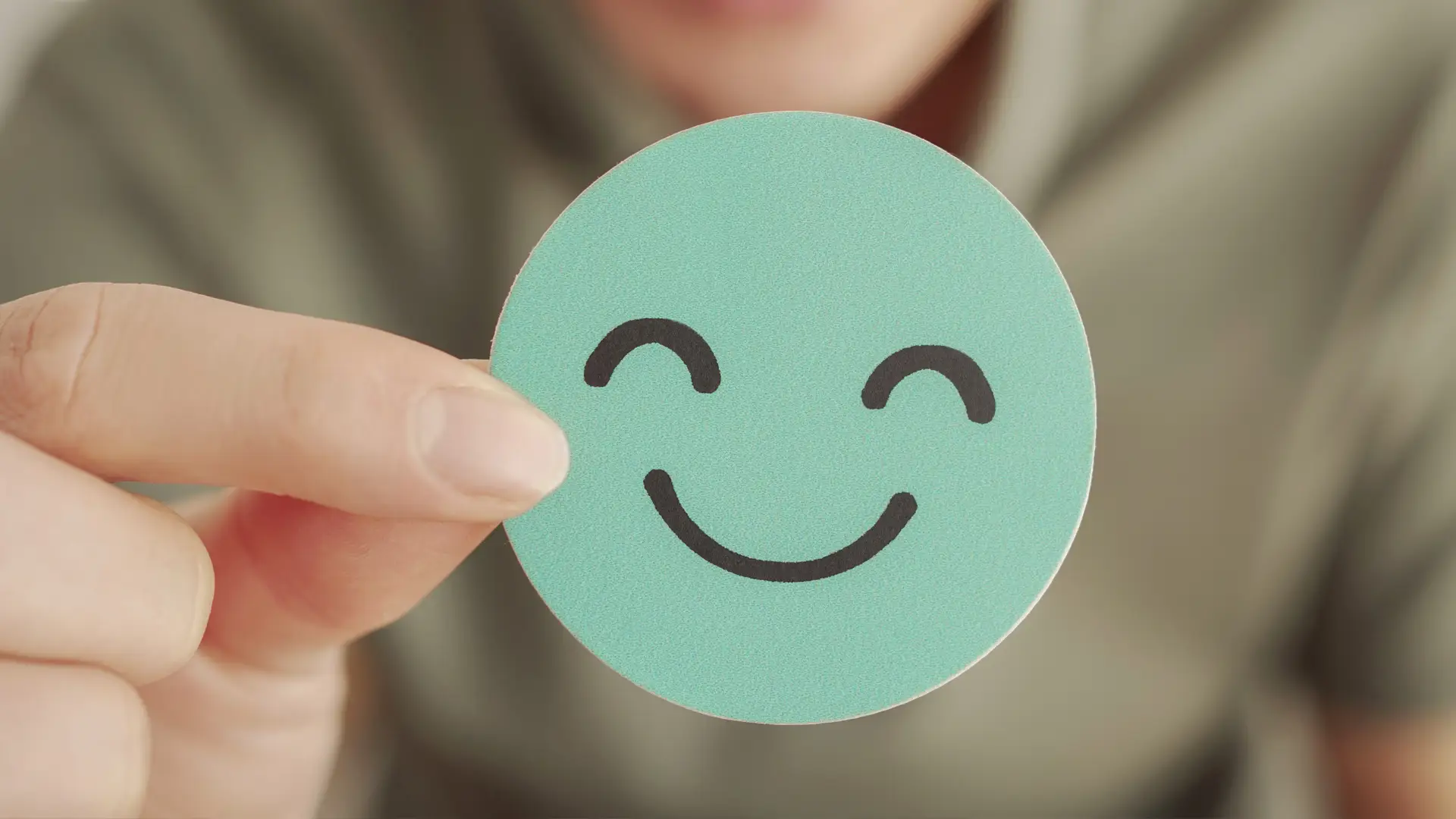 A person holding a teal smiley face card symbolising positive emotions and brand connection — representing how IC Creative Design helps Sunshine Coast businesses choose uplifting, memorable names.